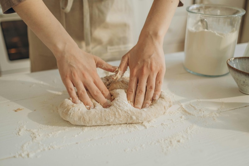 Hands kneading sourdough bread dough on a floured surface with milk in the background