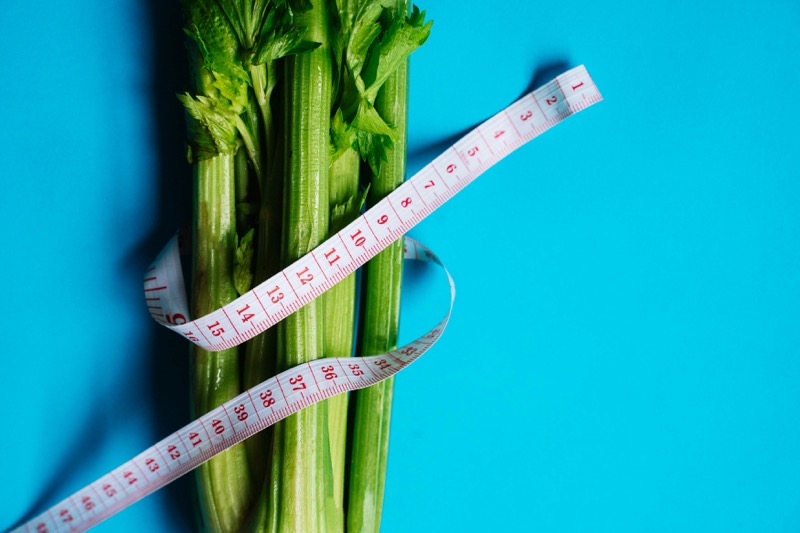 Weight Loss - Fresh celery with measuring tape representing healthy weight management